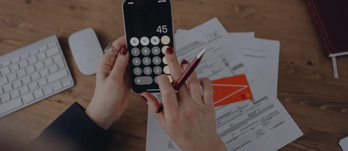 Hands using a phone calculator over tax papers on a desk.