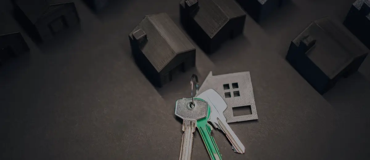 Dark gray model houses and a set of keys on a dark surface.
