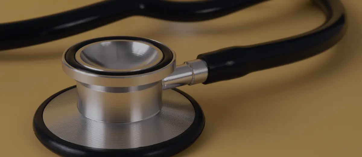 A silver stethoscope with black tubing lying on a yellow surface.