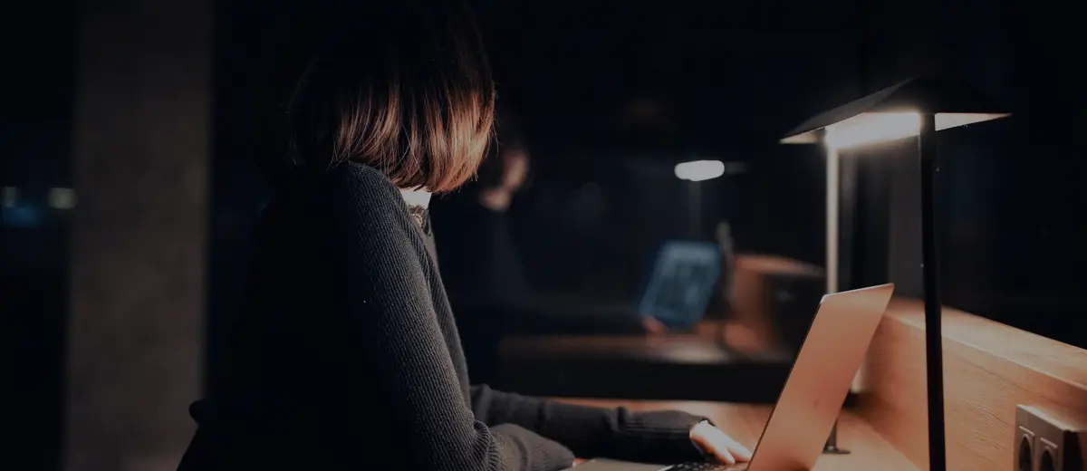 A person working on a laptop at night under a desk lamp.
