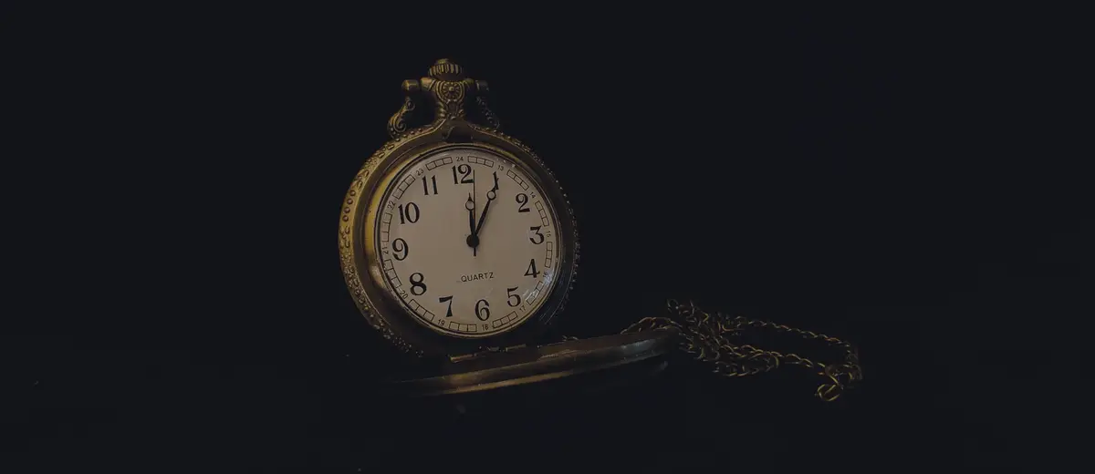 A gold pocket watch and its chain on a dark background.