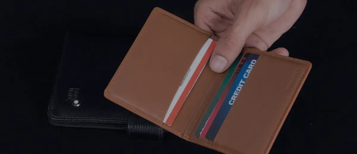 A hand pulling a card from a brown leather wallet.
