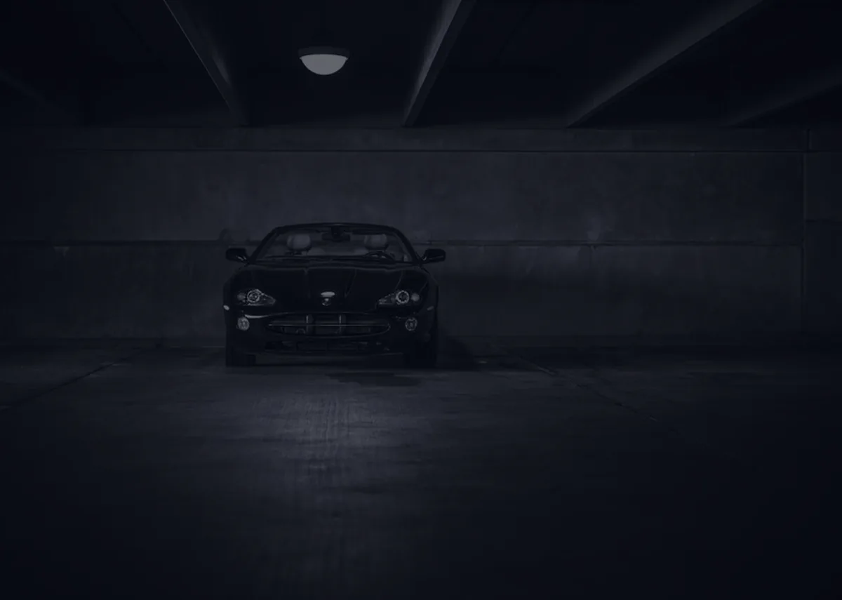 A car in a dark garage with headlights on, representing auto insurance.