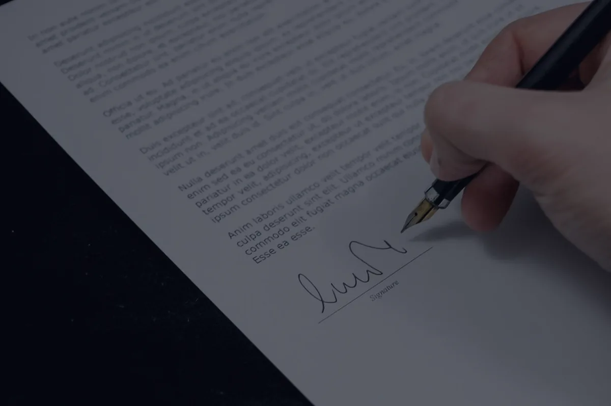 A fountain pen signing a document on dark, representing beneficiary designations.