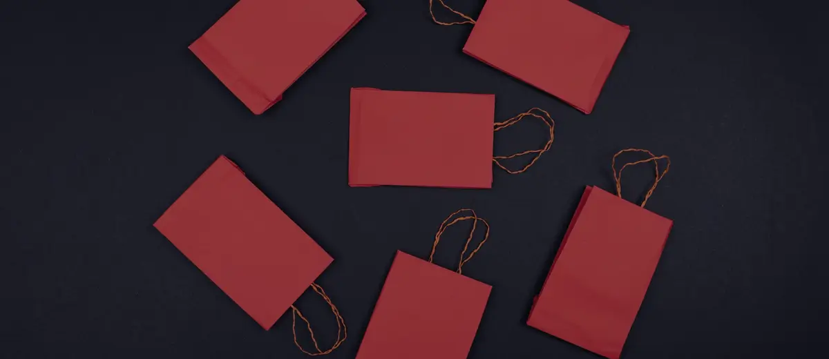 Six red paper shopping bags scattered across a black background.