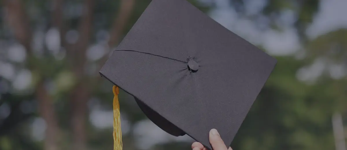 A hand holding up a black graduation cap outdoors.