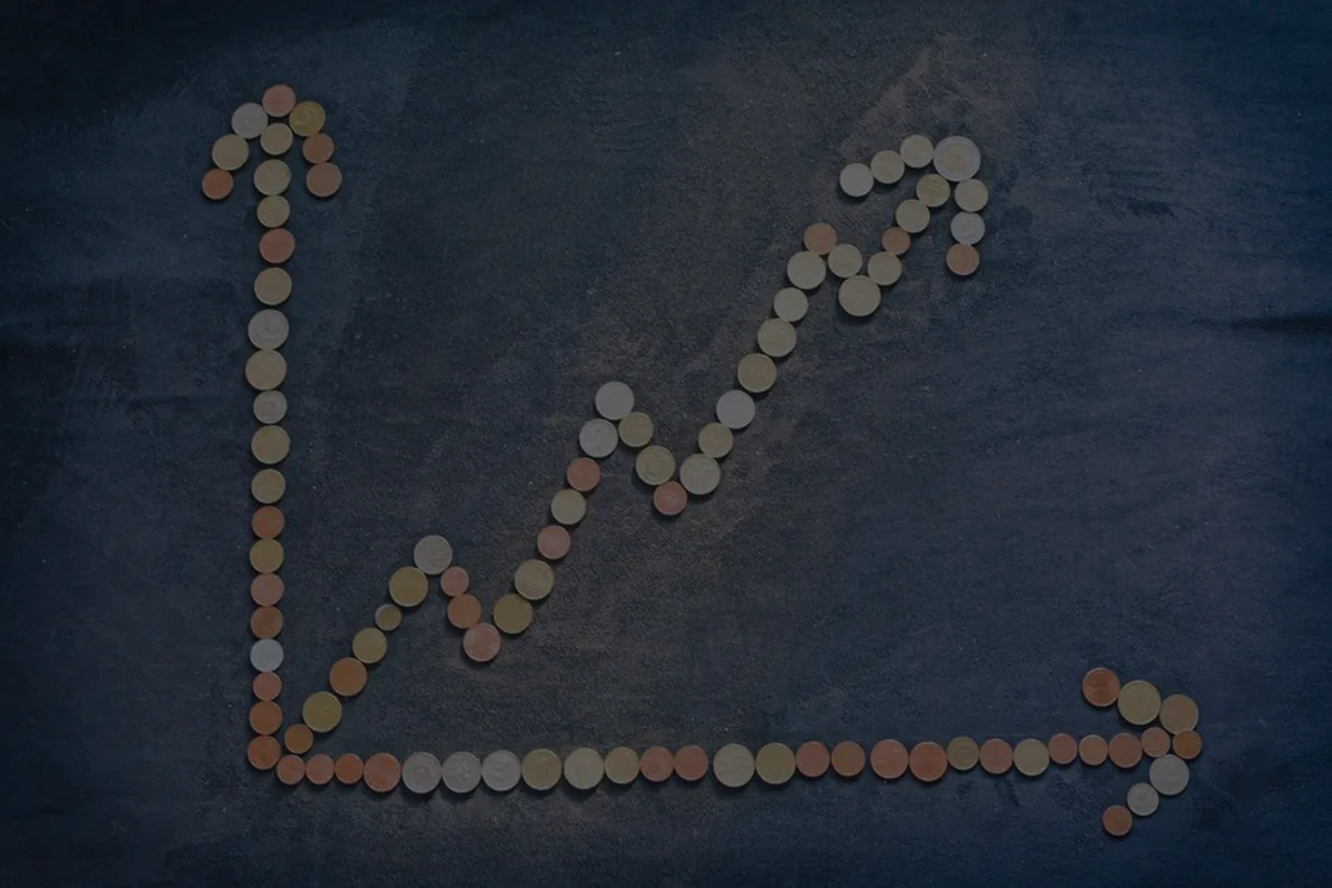 Coins arranged as an upward arrow on dark slate, representing capital gains on investments.