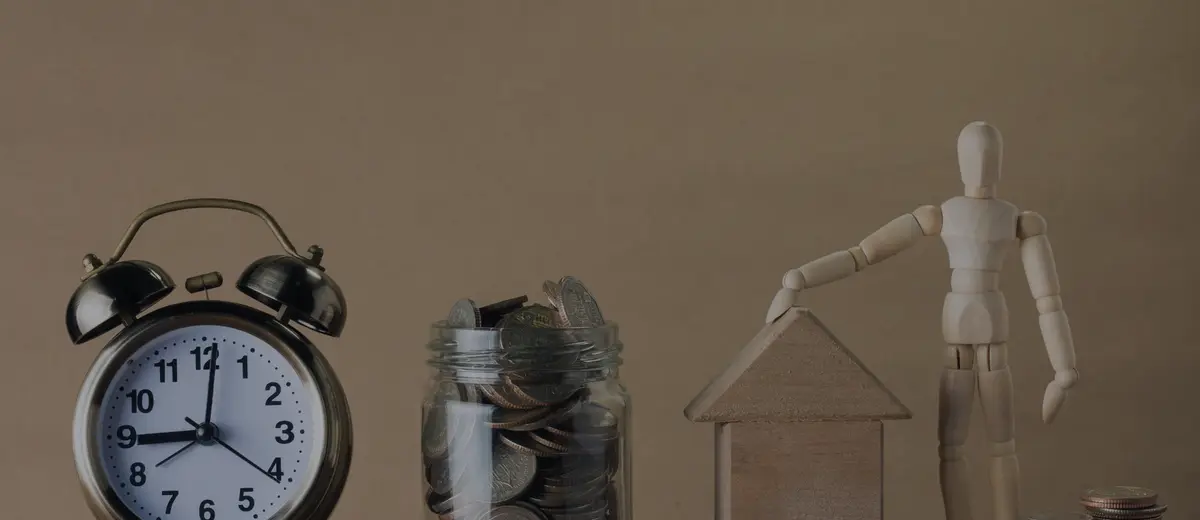 An alarm clock beside a jar of coins and a small wooden house.
