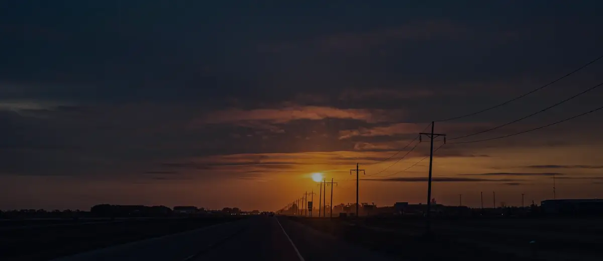 A two-lane road running toward a dark orange sunset.