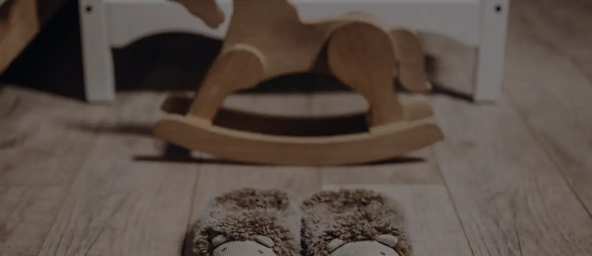 A wooden rocking horse and a pair of child's slippers on a wooden floor.
