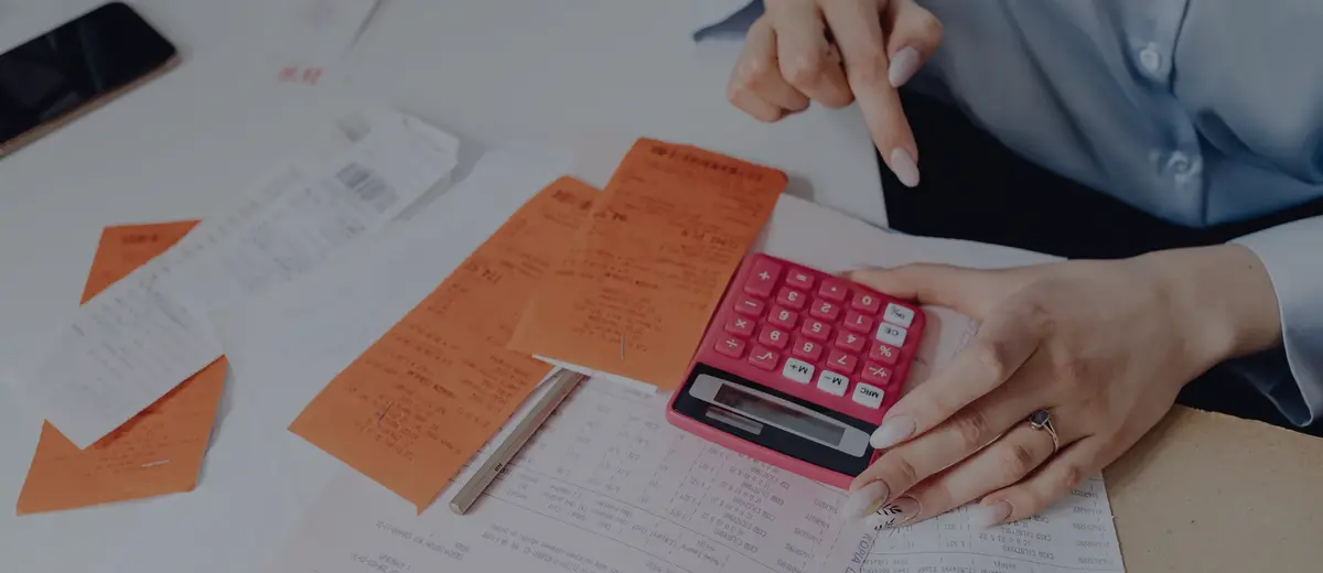 A person pointing at bills beside a pink calculator.