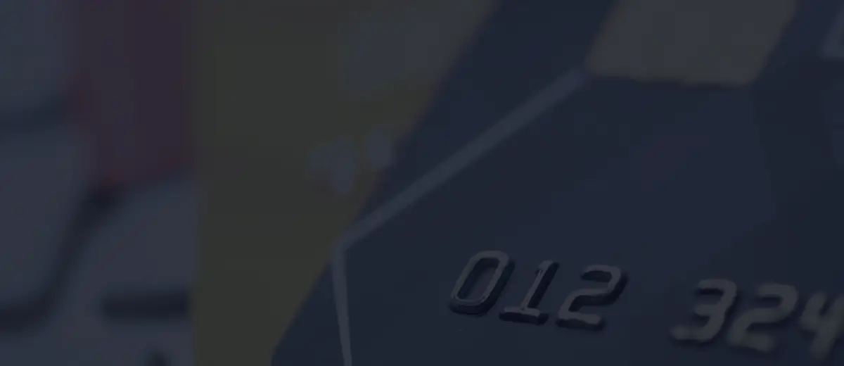 Close-up of the embossed number and chip on a dark payment card, with more cards blurred behind it.