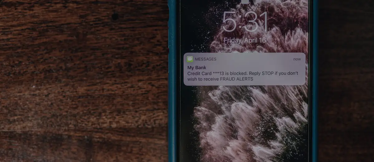 A smartphone showing a bank notification on a dark wooden table.