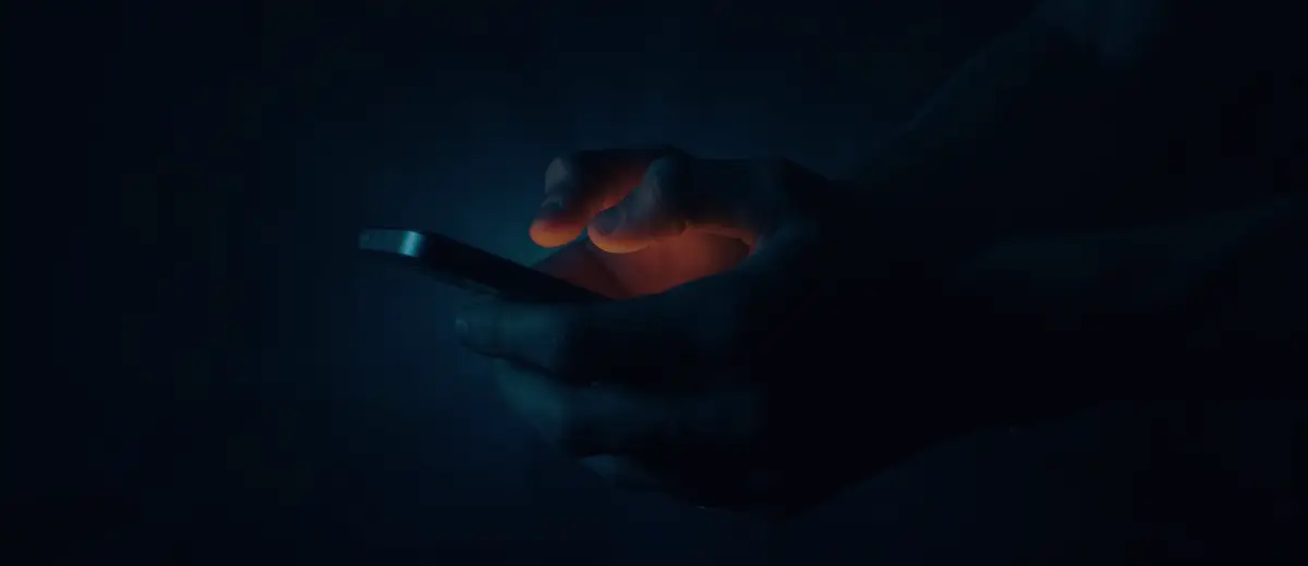 Hands holding a glowing smartphone in the dark.