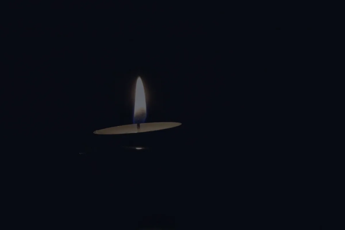 A single lit candle in somber dark, representing financial steps after the death of a spouse.