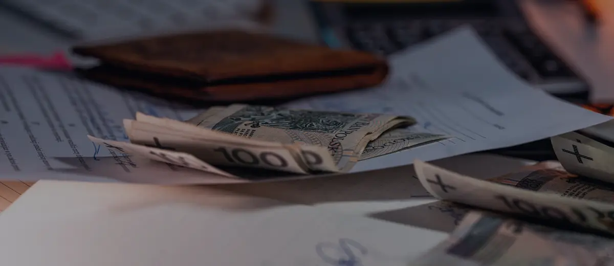 Cash, a wallet and bills spread across a desk.