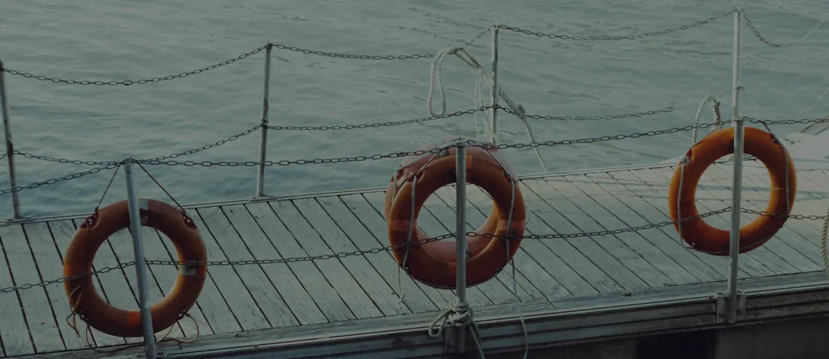 Three orange life rings hanging along a railing on a wooden dock by calm water.