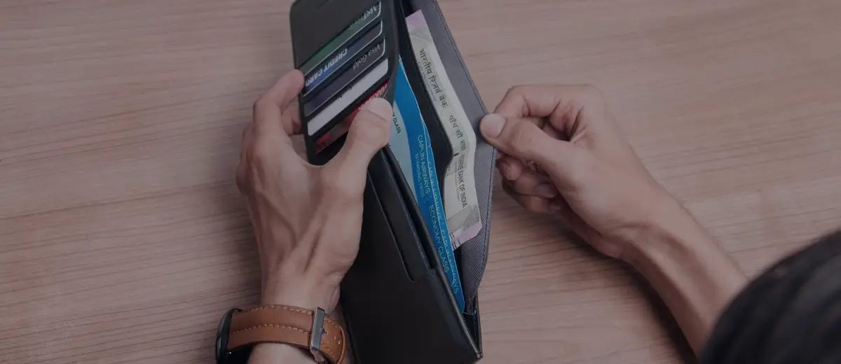 Hands pulling a card from a black wallet on a wooden surface.