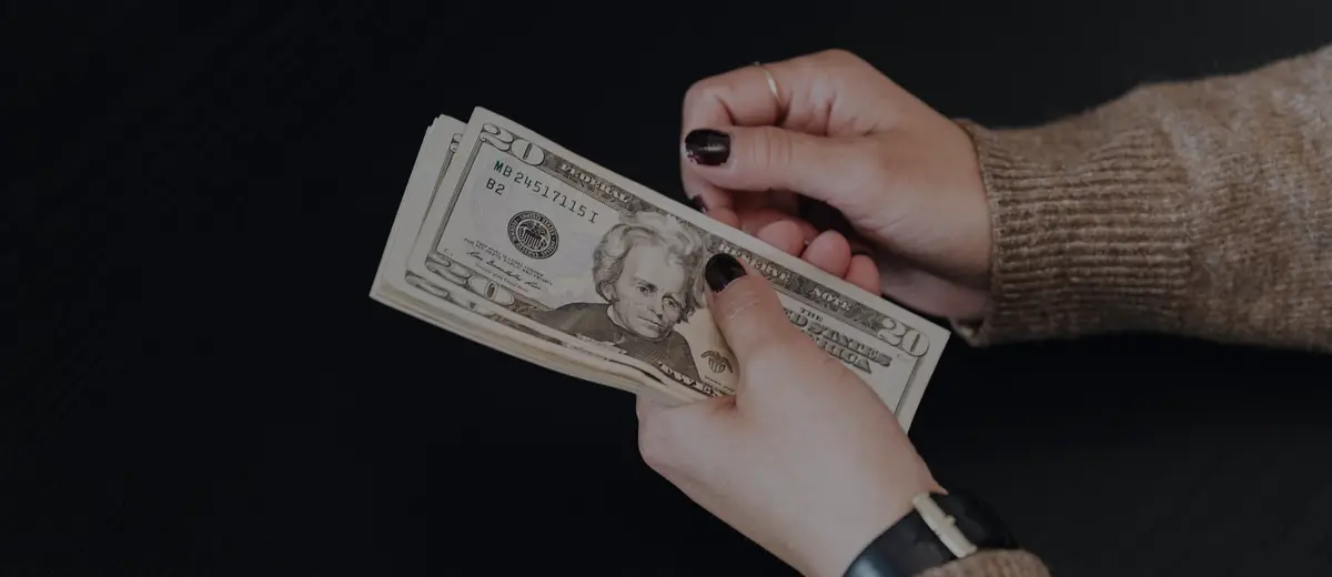 Hands counting a few twenty-dollar bills against a dark background.