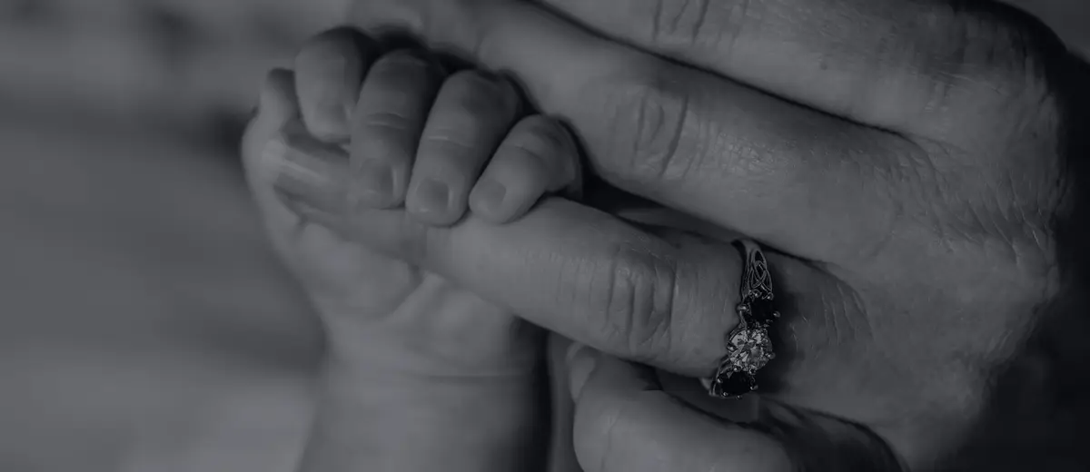 A baby's hand gripping an adult's fingers, in black and white.