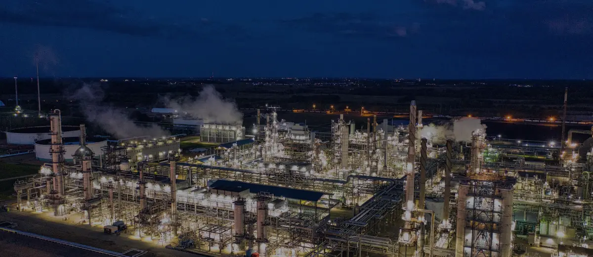 An oil refinery lit up at dusk under a deep blue sky.