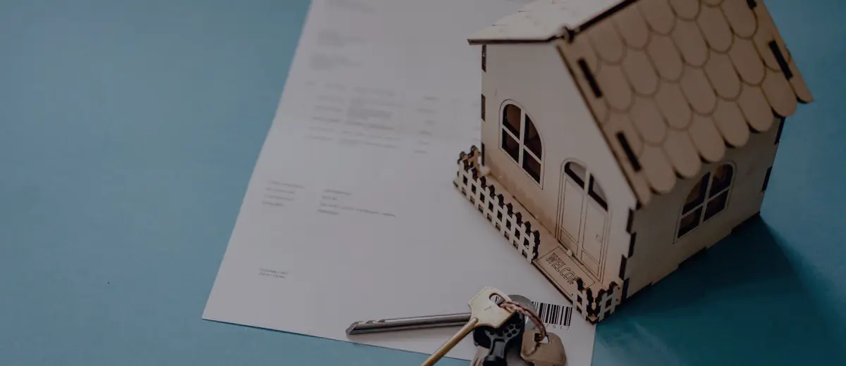 A small wooden model house with keys and papers on a blue desk.