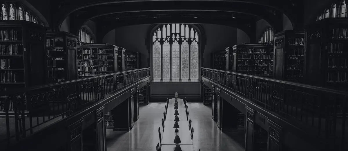 A grand library hall with a long reading table and tall shelves, in black and white.