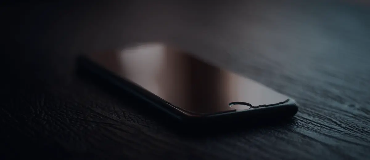 A smartphone with a dark screen on a wooden table.