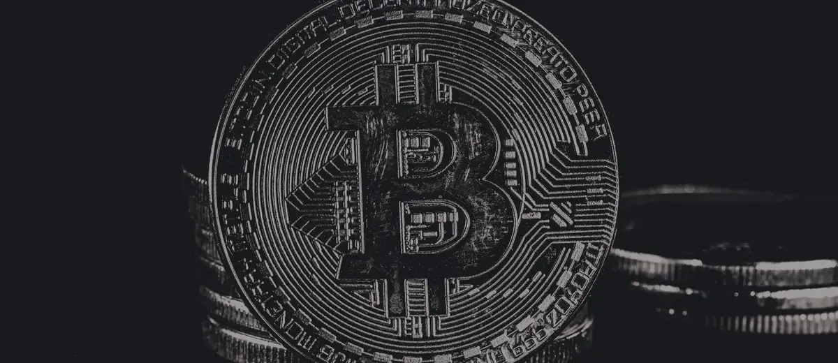 A silver bitcoin coin standing on a dark surface.