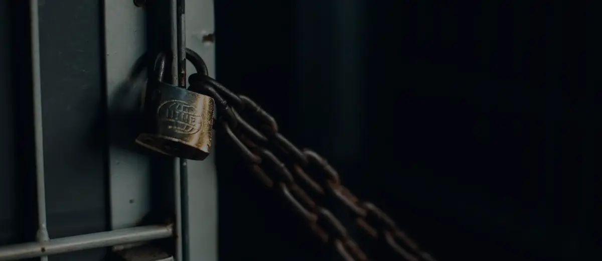 A worn padlock and chain on a dark metal gate.