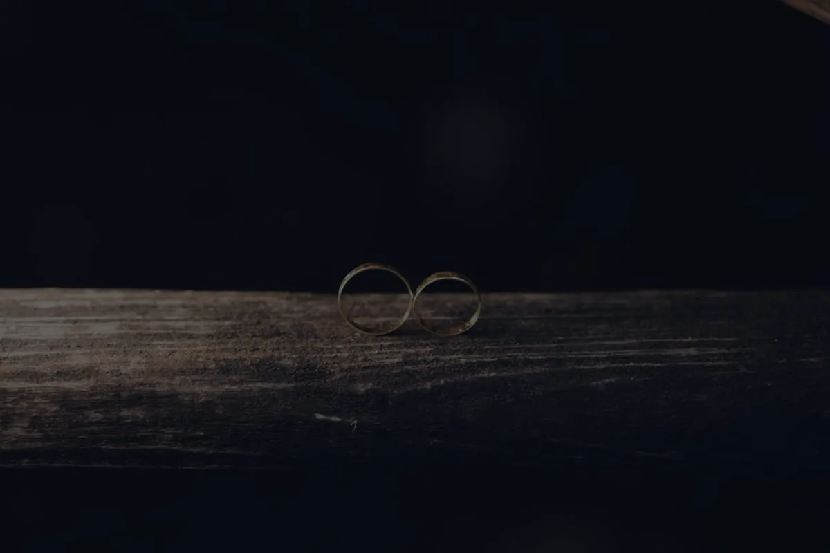 Two wedding rings on dark wood, representing combining finances after marriage.