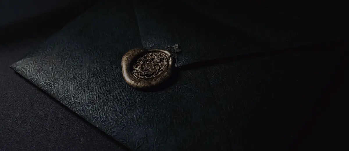 A black envelope sealed with a gold wax seal on a dark surface.