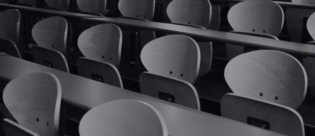 Rows of empty seats in a lecture hall, in black and white.