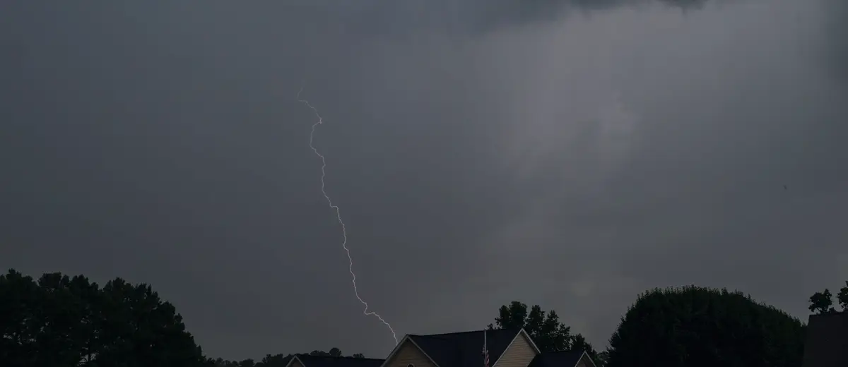 Lightning striking behind a house under dark storm clouds.