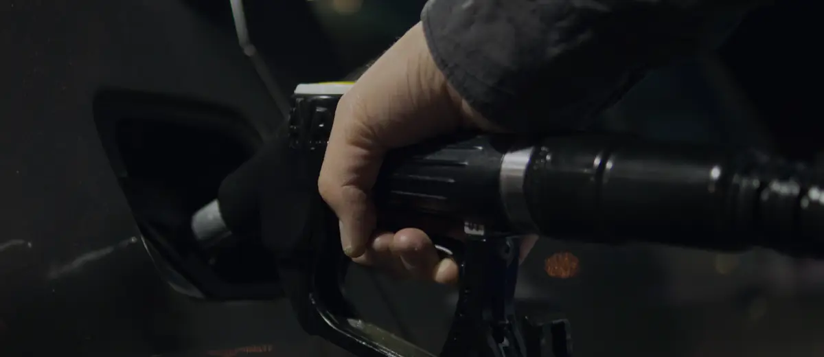 Close-up of a hand refueling a car with a gas pump nozzle at night.