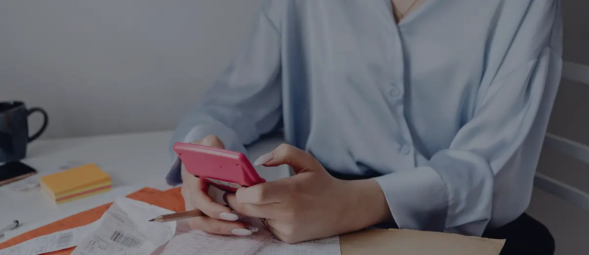 Hands holding a smartphone calculator over papers and receipts.
