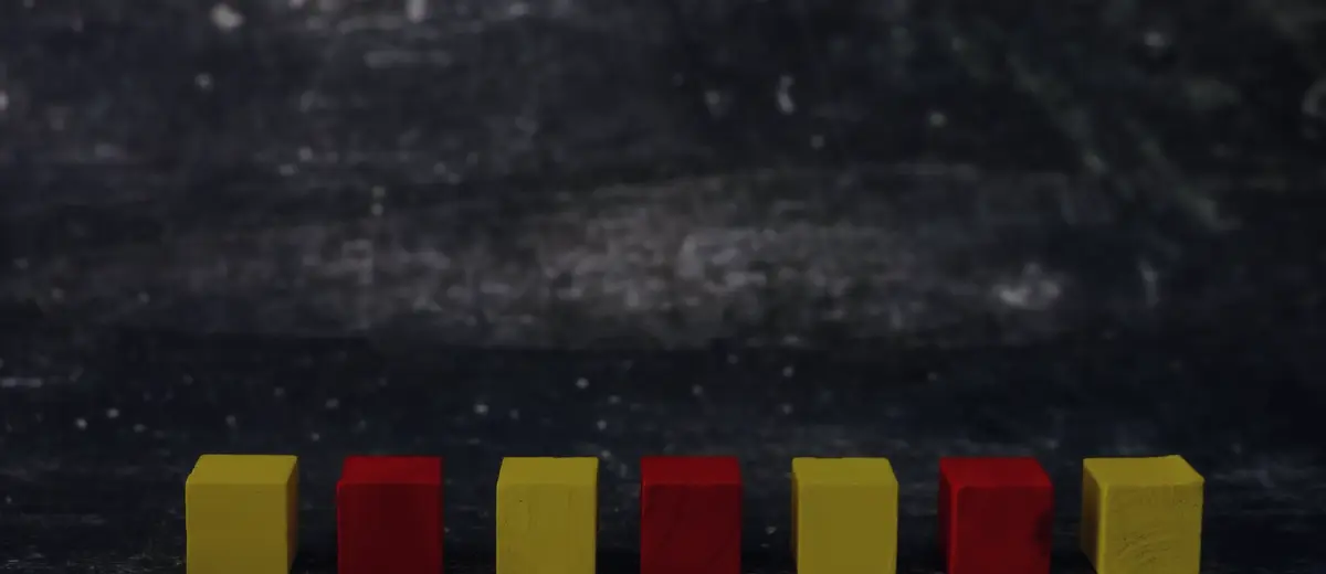 A row of red and yellow wooden toy blocks against a dark wall.