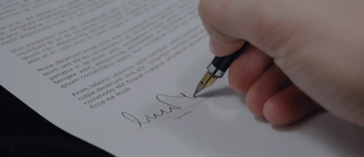 A hand signing a document with a fountain pen.