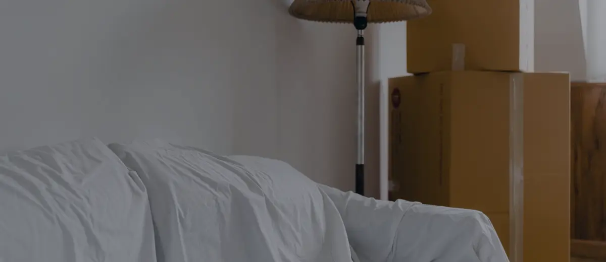Moving boxes and furniture under a sheet in an empty room.