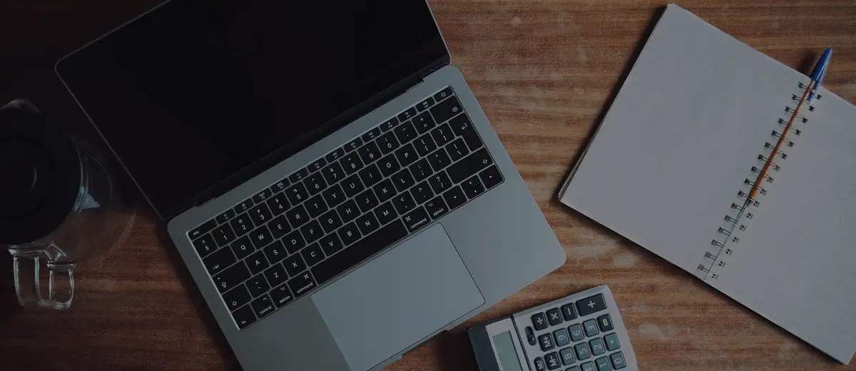 A laptop, calculator and notebook on a wooden desk.