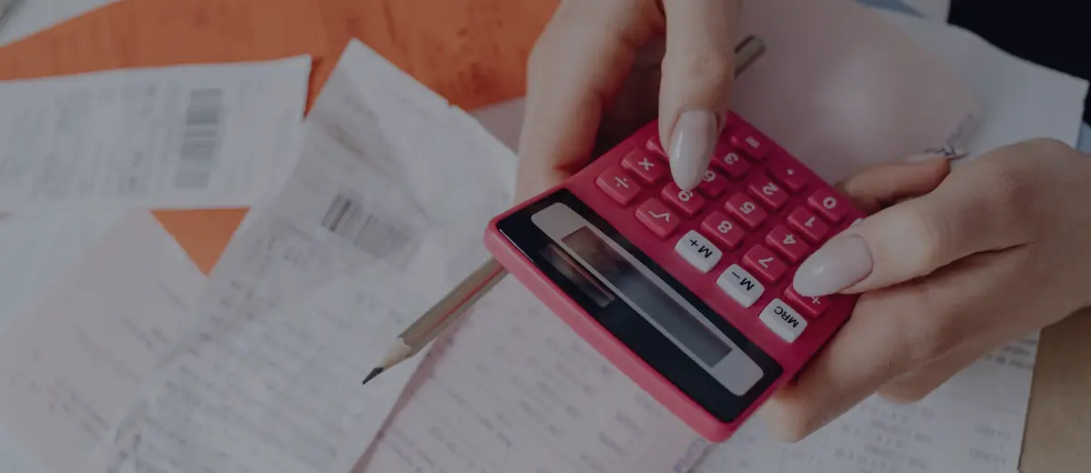 Hands using a pink calculator over a pile of bills.