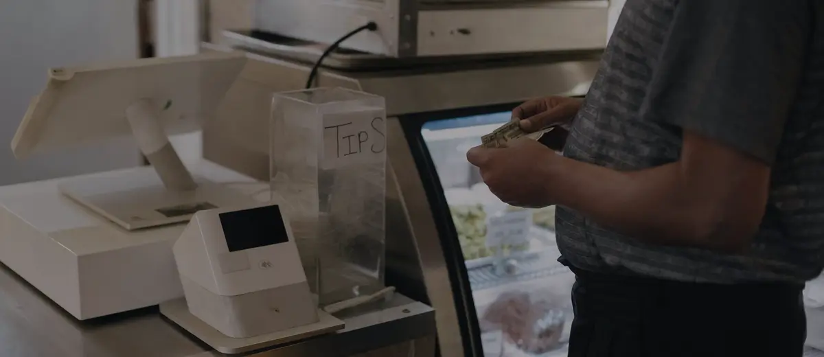 A tip jar beside a card payment terminal on a shop counter.