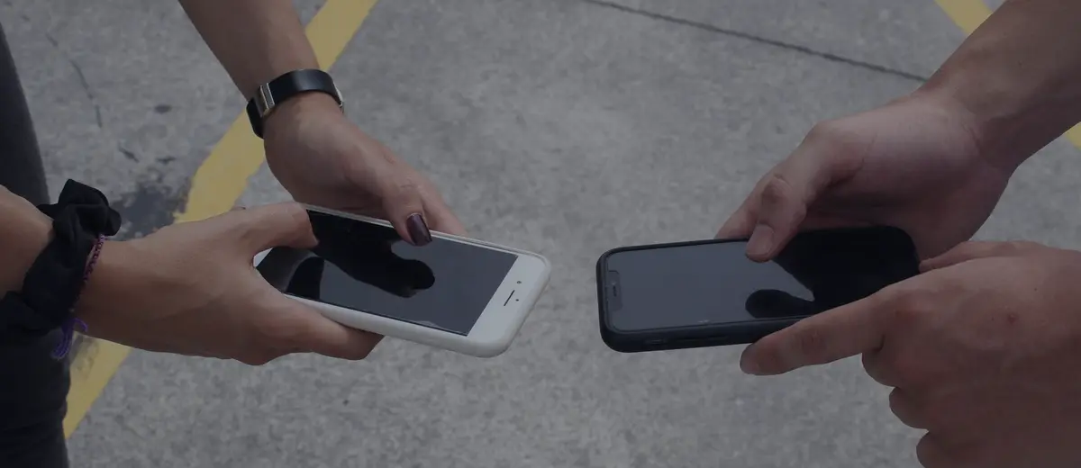 Two people's hands holding phones toward each other.