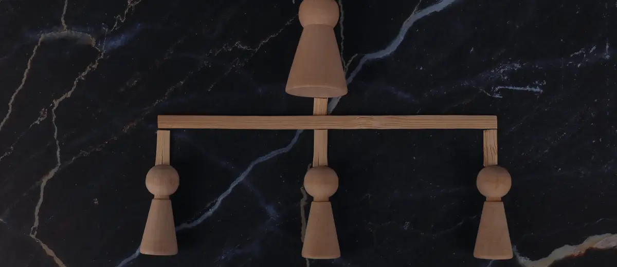 A small wooden balance with three figures on a dark marble surface.