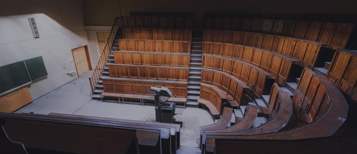 An empty wooden lecture hall with rows of seats rising toward the back.