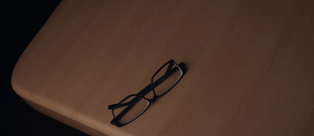 A pair of black eyeglasses resting on a wooden table.