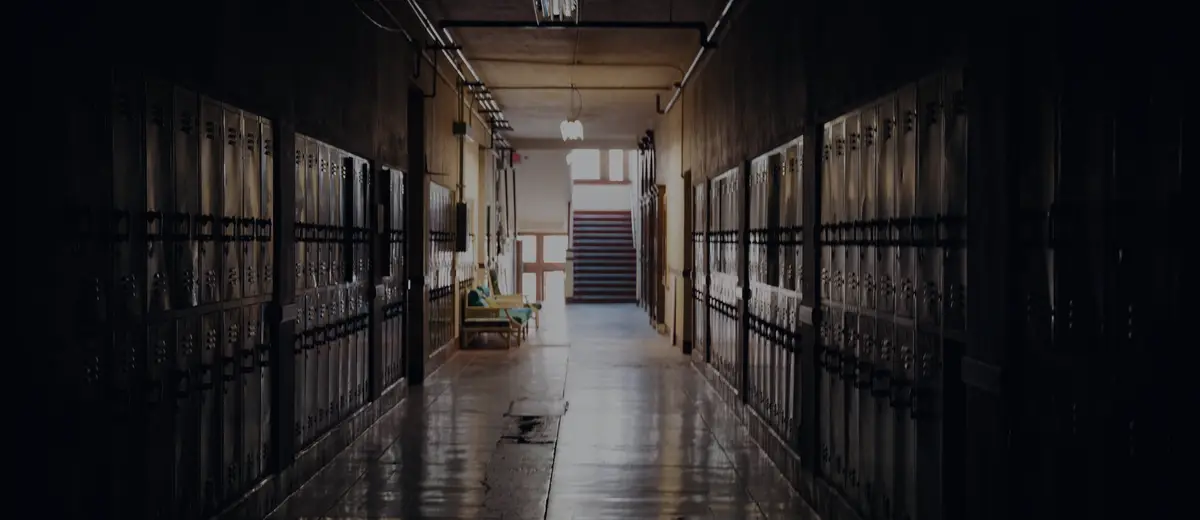 A dark, empty school hallway lined with lockers, lit at the far end.
