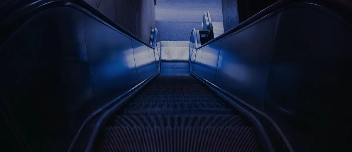 Looking down a long escalator lit in blue in a dark station.