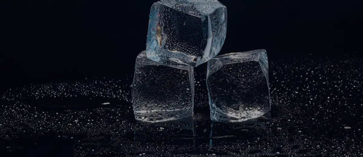 Three ice cubes melting on a dark surface, with drops of water around them.