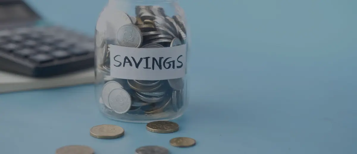 A glass savings jar filled with coins beside a calculator.